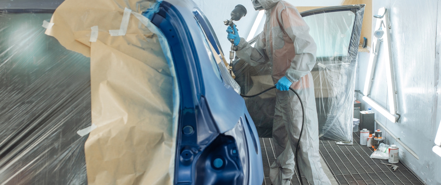 Peintre automobile appliquant peinture sur voiture bleue.